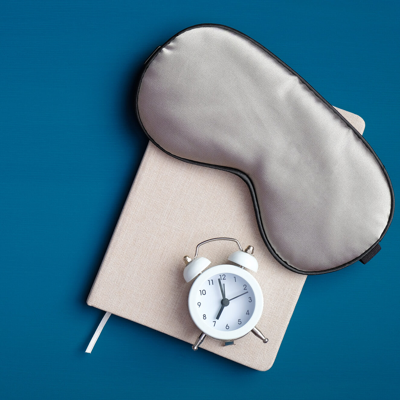 Flat lay composition with sleep eye mask, dream book and alarm clock on dark blue background. Healthy sleeping concept.